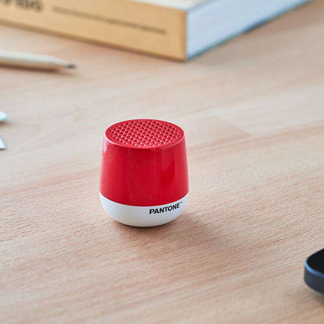 Red Lexon Speaker on a wooden surface with a phone and paper in the background.
